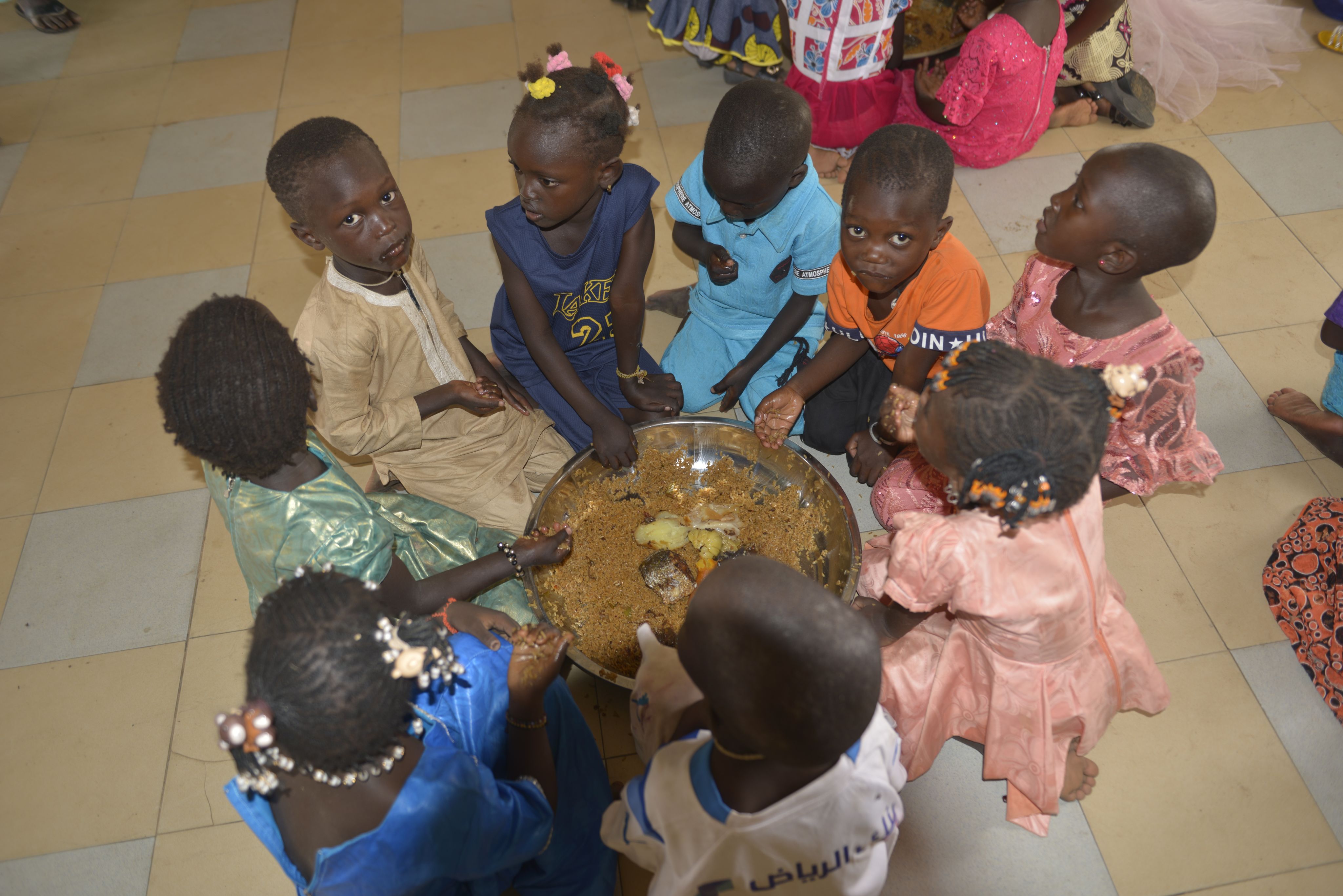 Les enfants partagent les repas autour de grands plats.